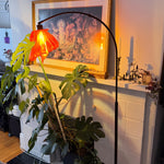 Arc Arise Standing Lamp with black base, lit beside a fireplace