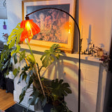 Arc Arise Standing Lamp with black base, lit beside a fireplace