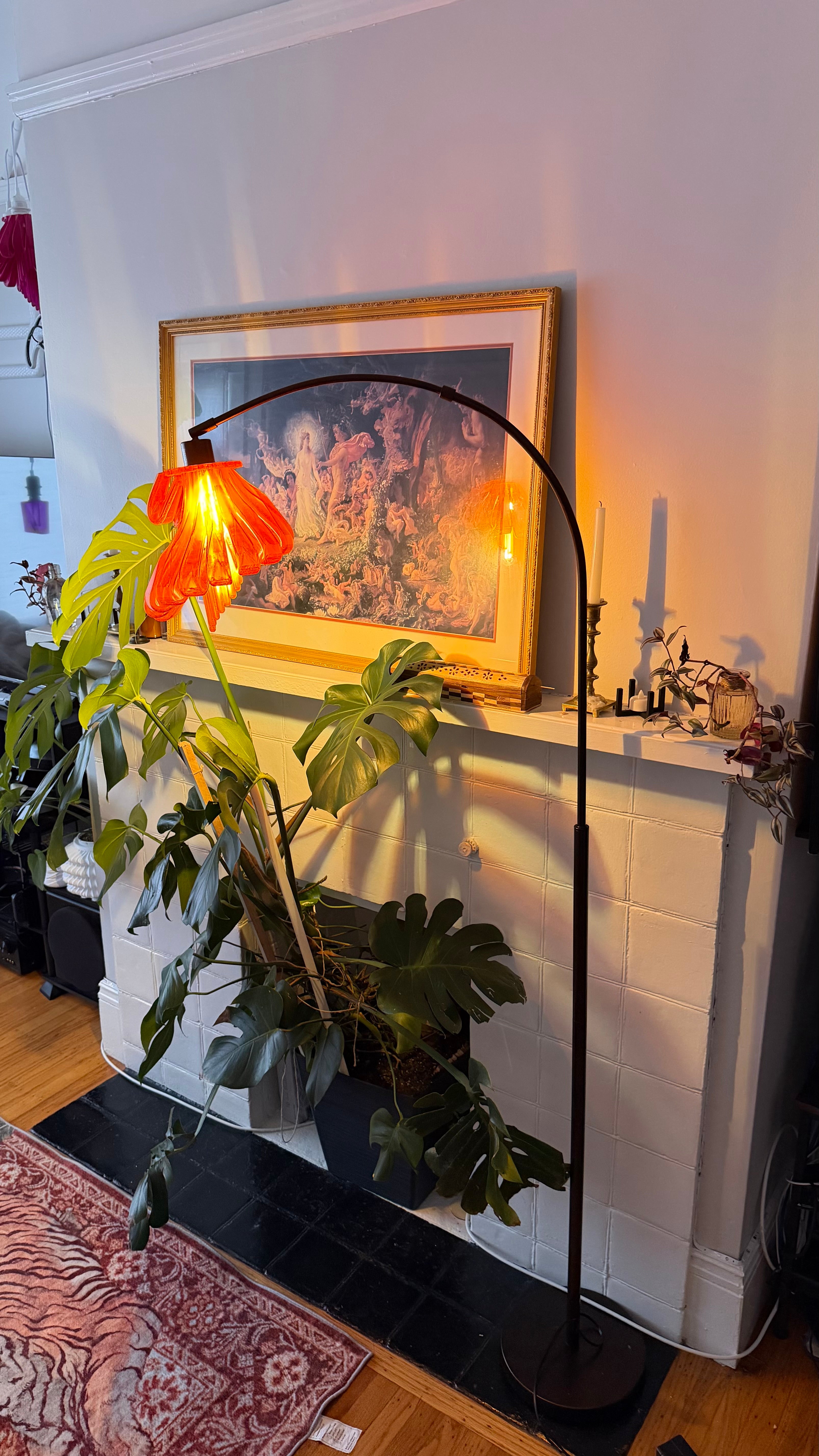 Arc Arise Standing Lamp with black base, lit beside a fireplace